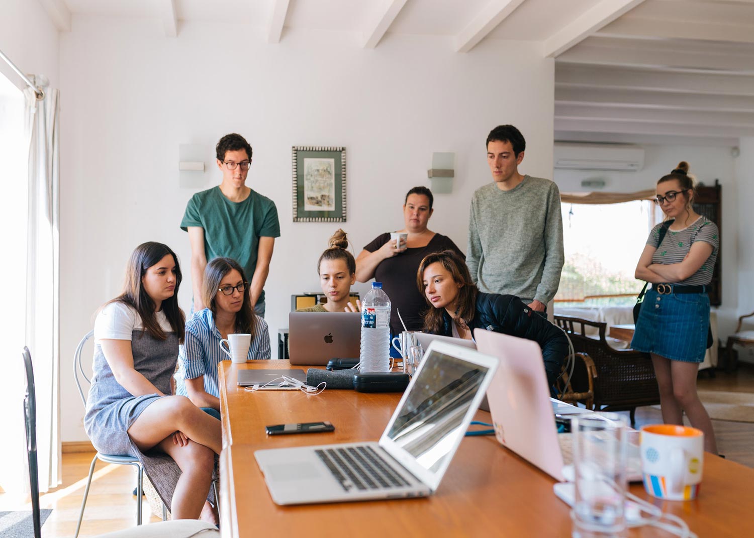 group of people gatheredaround a macbook at the head of a table